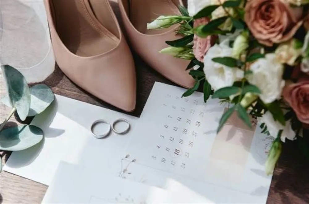 Elegant wedding setup with blush heels, a bouquet, rings, and a calendar—hinting at a special date and vows.