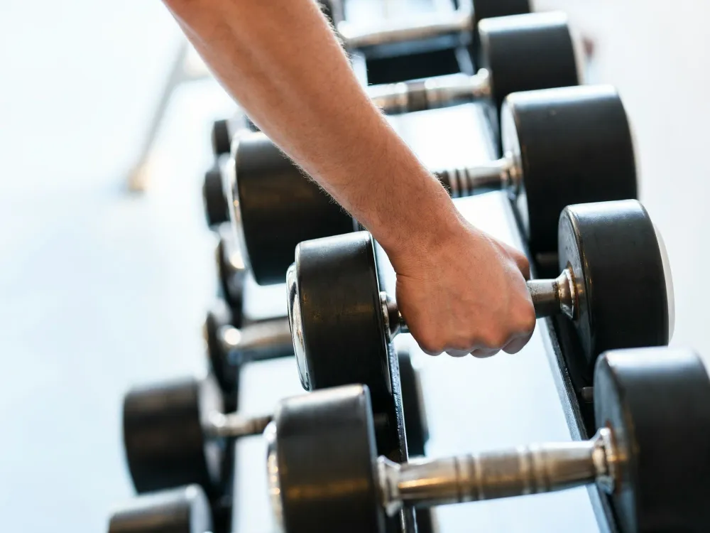 A person gripping a dumbbell in a gym, with row of free weights lined up on a rack near them.