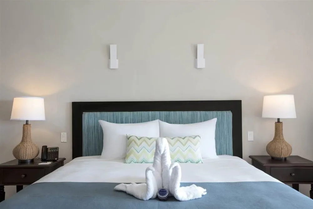 A modern hotel bedroom with a neatly made bed, bedside lamps, and a folded towel swan on the sheets.