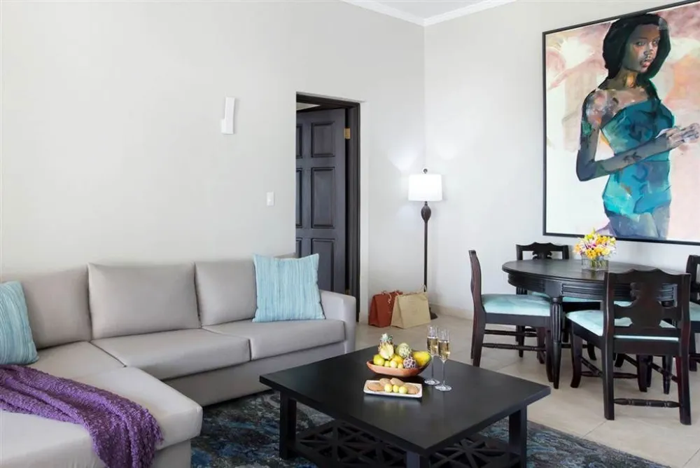 A modern living room with a gray sectional, teal throw pillows, and a purple blanket; a black coffee table, dining set, and a large wall art of a woman.