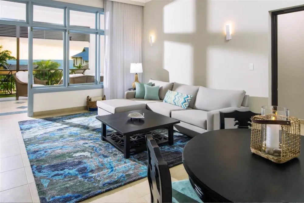 A bright, modern living room with a gray sofa, turquoise accents, a blue patterned rug, and a view of a balcony through large windows.