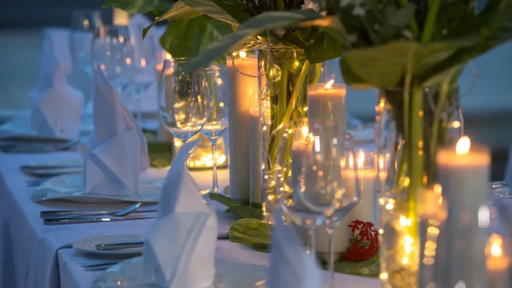 A candlelit outdoor dining table with wine glasses and greenery glowing under warm lights.