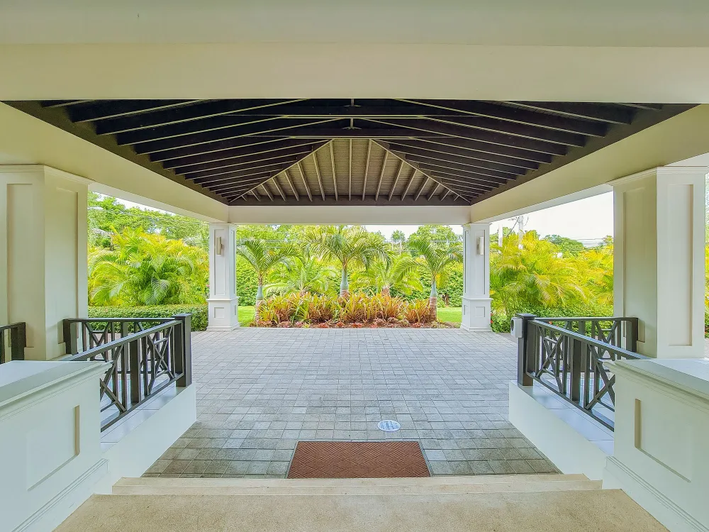 A covered villa porch with a tiled floor, wooden ceiling beams, and a view of lush tropical gardens and palm trees.