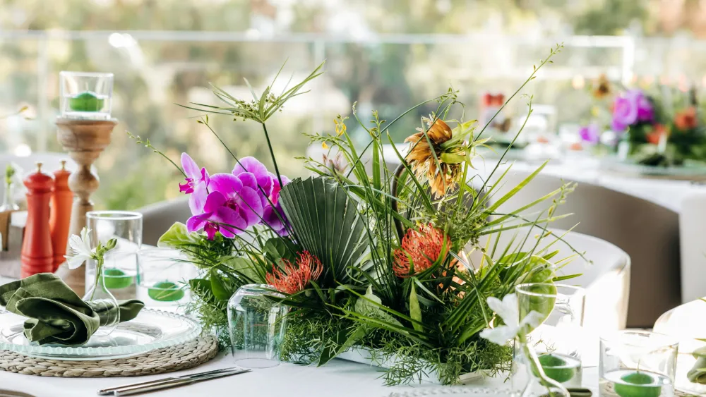 A bright garden scene with a bouquet of flowers in a vase, lanterns, and a sunlit table setting in soft focus, outdoors.