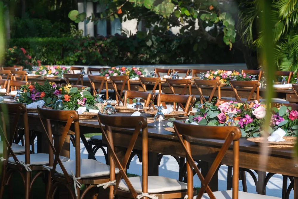 A sunny outdoor café scene with wooden tables and chairs, people dining under trees by a street—pleasant, bustling, and relaxed.
