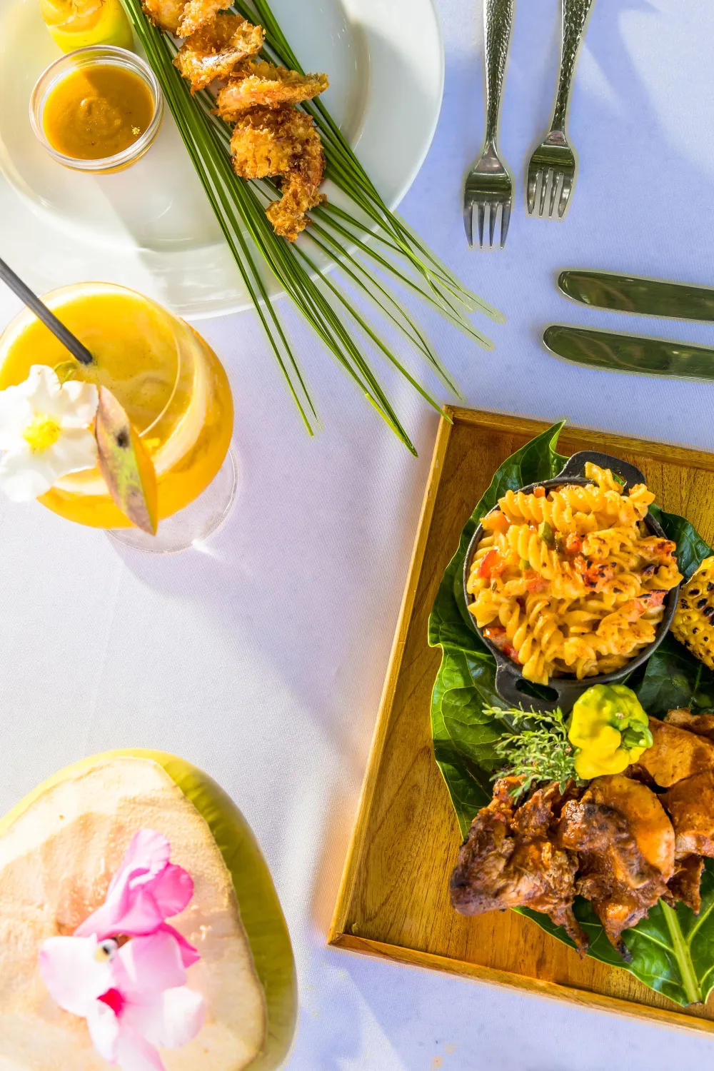 A vibrant brunch: fried shrimp skewers, fresh greens, bright orange mango salsa, a grilled meat dish on a wooden plate, citrus drinks, and a pastel table setup.