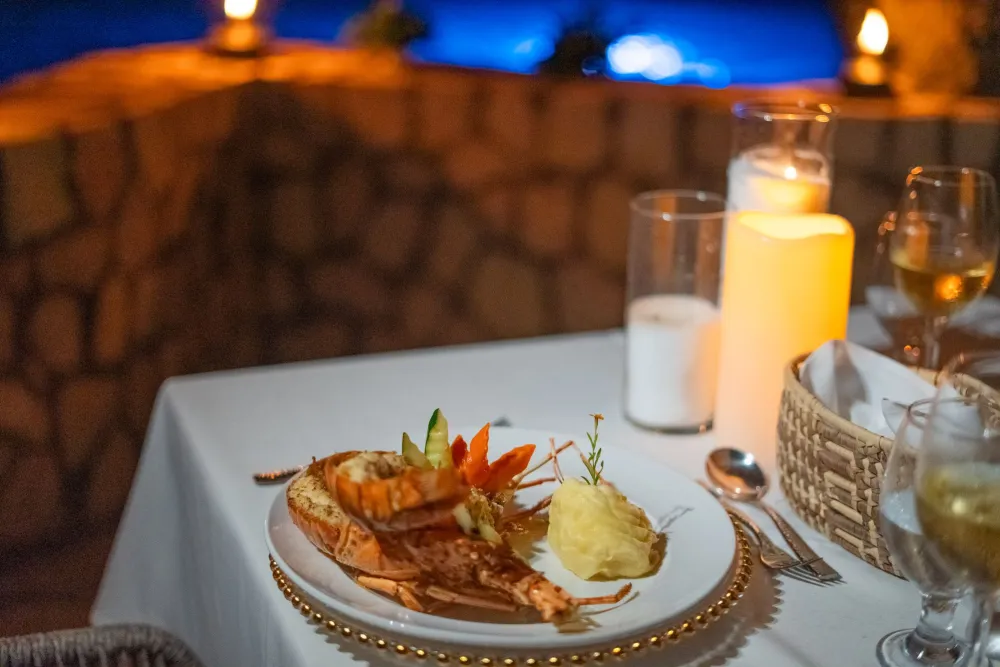 A romantic dinner setup with a lobster dish, mashed potatoes, candlelight, and wine glasses on a white tablecloth, soft evening ambiance.