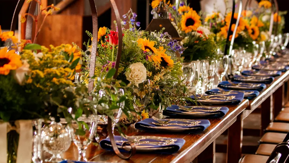 A long dining table set for a formal feast with colorful flower centerpieces, folded napkins, and glassware—elegant and festive.