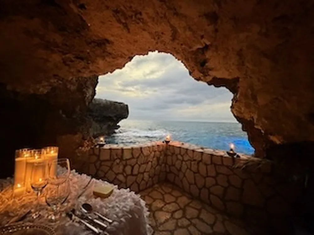 The view from inside The Cave through its stone mouth to the open Caribbean Sea, with candles on the low stone wall.