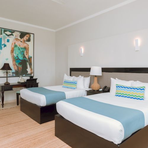 Two twin beds in a bright hotel room with a large artwork, nightstands, lamps, and a beige rug, arranged neatly.