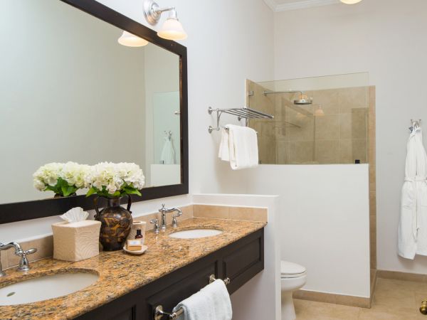 A modern bathroom with a double vanity, granite countertop, large mirror, and a walk-in shower; white towels, flowers, and neutral tiles add a classy touch.