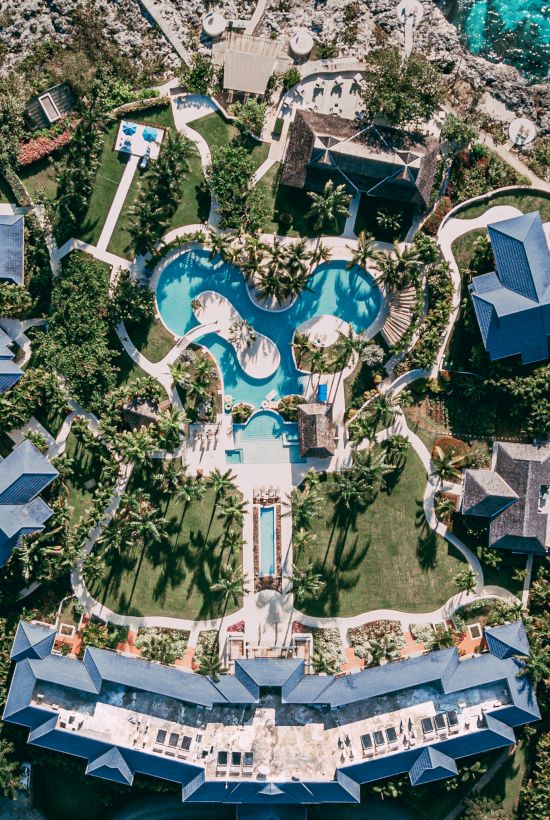 Aerial view of a resort with a large, winding pool shaped like a heart or clover, surrounded by lush greenery and buildings.