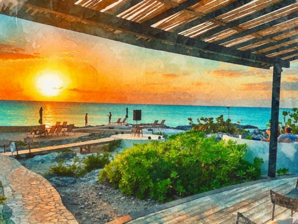 A seaside resort terrace with lush plants, lounge chairs, and a glowing sunset over the turquoise ocean, under a wooden shelter.