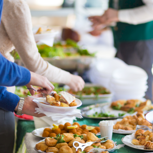 A group of people serving food at a communal buffet line with various dishes laid out on a table.