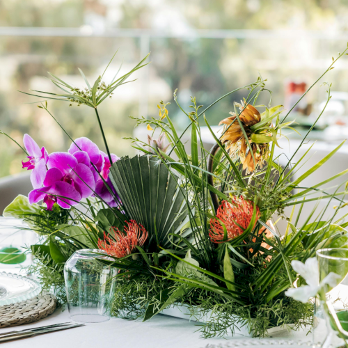 A bright garden scene with a bouquet of flowers in a vase, lanterns, and a sunlit table setting in soft focus, outdoors.