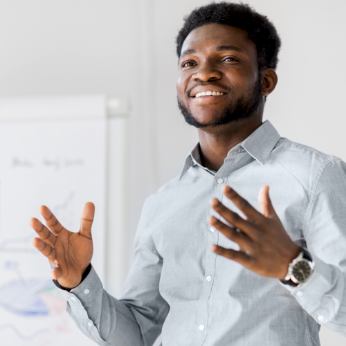 A man presents and gestures in front of a chart, explaining data on a whiteboard.