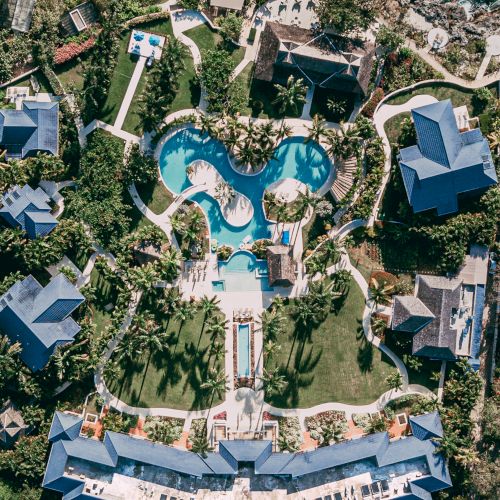 Aerial view of a resort with winding pools, palm trees, and surrounding villas, forming a heart/flower-like layout.