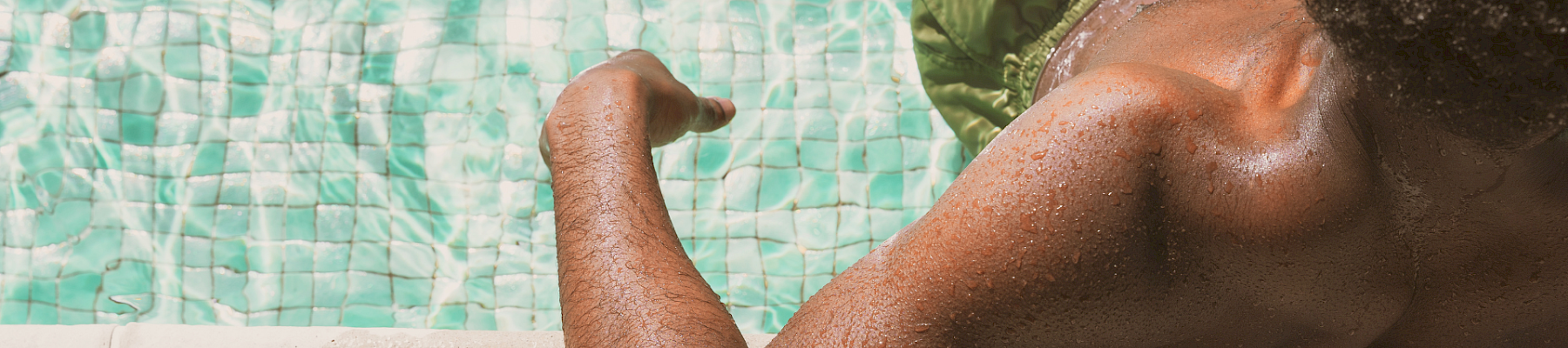A person resting by a pool edge, arm and shoulder visible, soaking up sun and water reflections.
