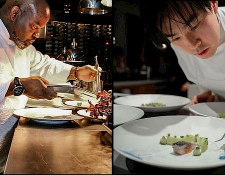 The image shows two chefs plating food at a restaurant, carefully garnishing dishes on white plates.