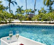 A sunny poolside scene with palm trees, two champagne flutes, and a fruit plate resting on a wicker table.