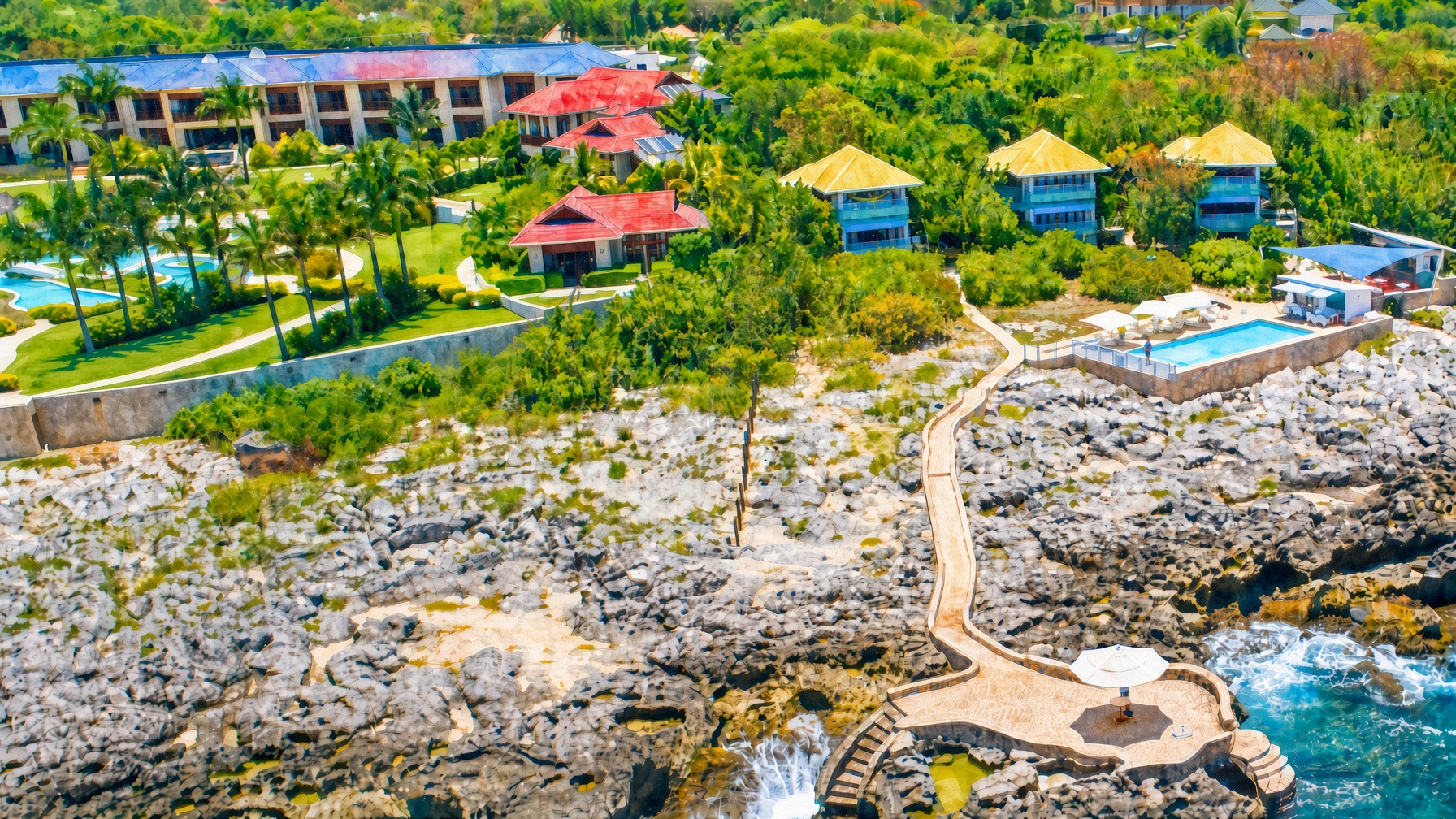 Aerial view of a tropical resort with colorful buildings, pools, and a beach with a wooden walkway winding through rocks and sand.