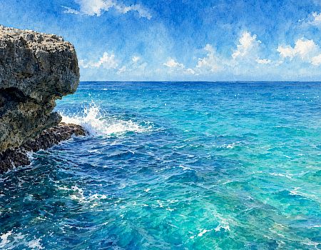 Waves crash against a rocky cliff as turquoise ocean and a bright blue, cloud-dotted sky stretch to the horizon.